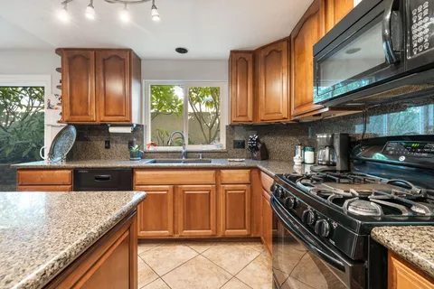 a kitchen with stainless steel appliances granite countertop a sink a stove and a wooden cabinets