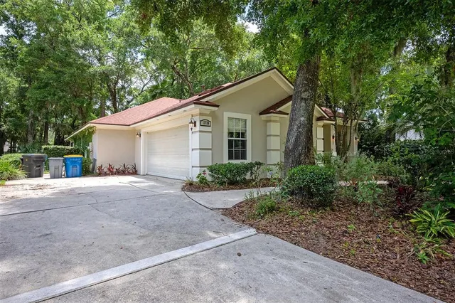 a white house with a small yard plants and large trees