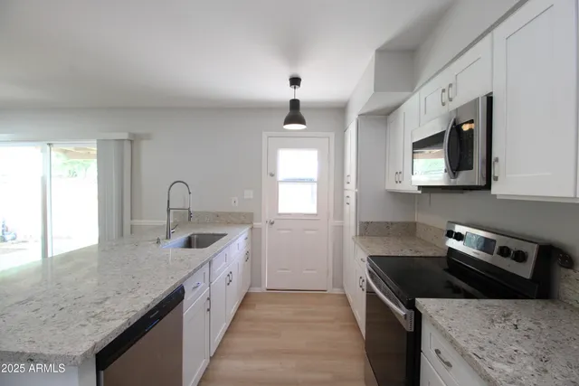 a kitchen with granite countertop a sink dishwasher a stove and a microwave oven with white cabinets