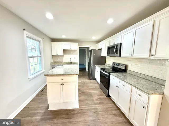 a large kitchen with granite countertop a sink a counter space stainless steel appliances and cabinets