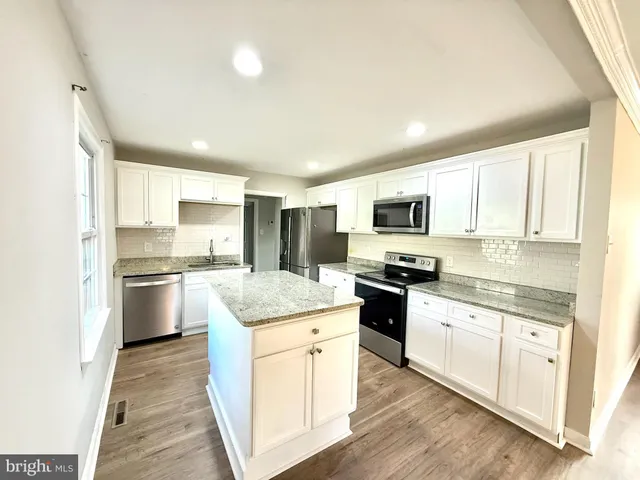 a kitchen with stainless steel appliances granite countertop a stove top oven a sink a refrigerator white cabinets and wooden floor