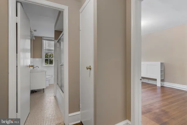a view of a hallway with wooden floor a glass door and a bathroom