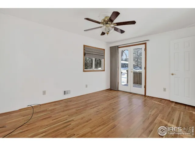 a view of an empty room with wooden floor and a ceiling fan
