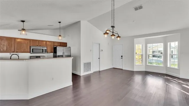 a view of an empty room with kitchen and a window
