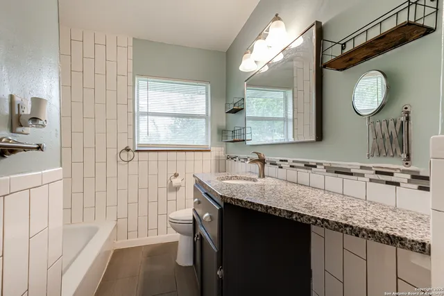 a bathroom with a granite countertop sink a large mirror a vanity and a bathtub