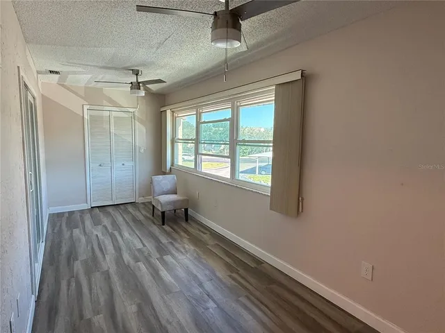 a view of a room with wooden floor a ceiling fan and windows