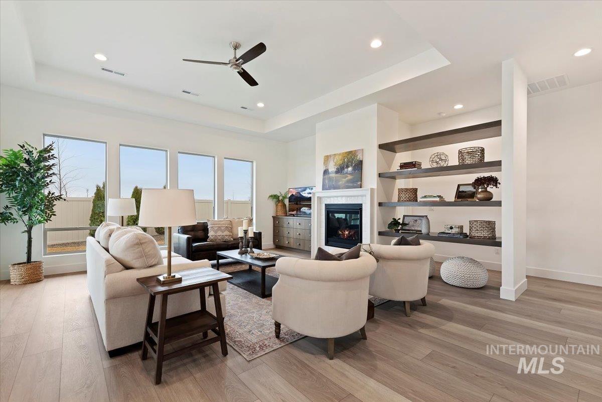 1297 Chena Street Middleton, ID 83644 - Photo 10 of 38 Living area with a tray ceiling, a ceiling fan, light wood-style flooring, a glass covered fireplace, and recessed lighting