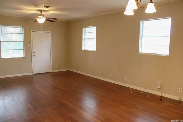 an empty room with wooden floor chandelier fan and windows