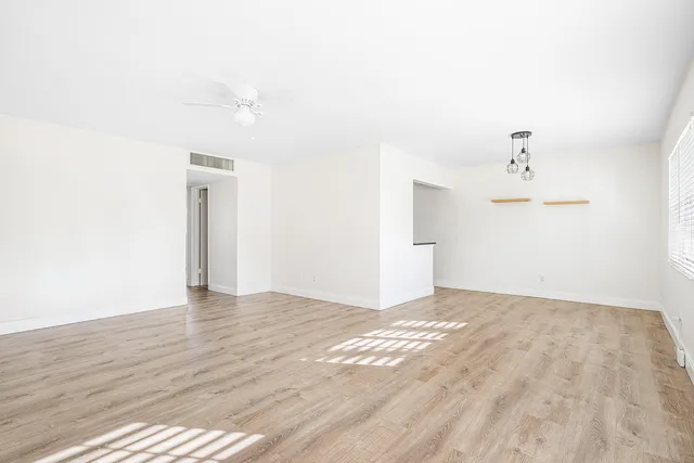 a view of an empty room with wooden floor and ceiling fan