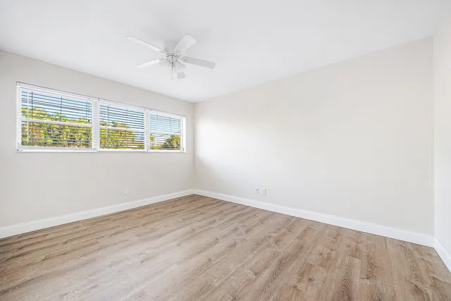 an empty room with wooden floor fan and windows