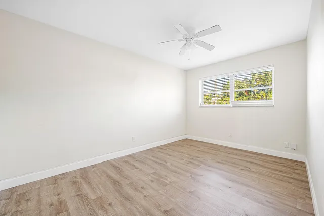 an empty room with wooden floor window and ceiling fan