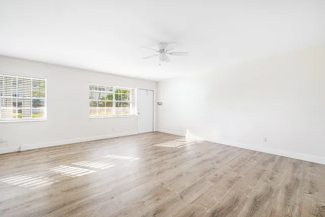 an empty room with wooden floor ceiling fan and windows