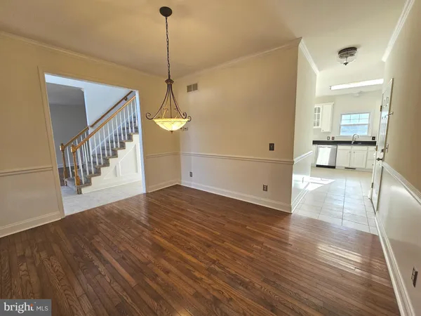 a view of an empty room and kitchen view with wooden floor and a window
