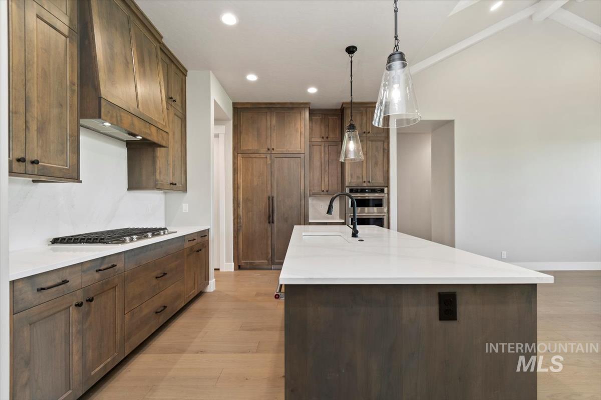 7353 Powell Place Eagle, ID 83714 - Photo 11 of 45 Kitchen featuring a kitchen island with sink, decorative light fixtures, light stone counters, light wood-type flooring, and recessed lighting