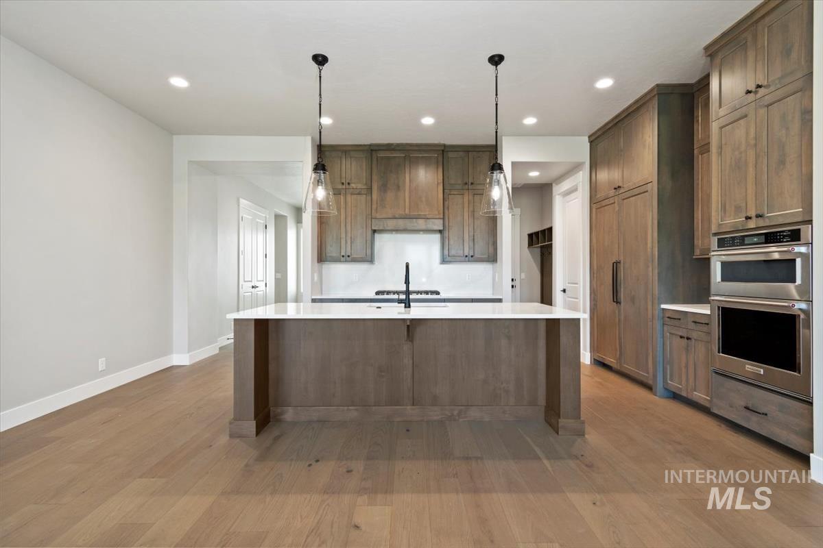 7353 Powell Place Eagle, ID 83714 - Photo 12 of 45 Kitchen featuring hanging light fixtures, recessed lighting, appliances with stainless steel finishes, light stone counters, and light wood-style floors