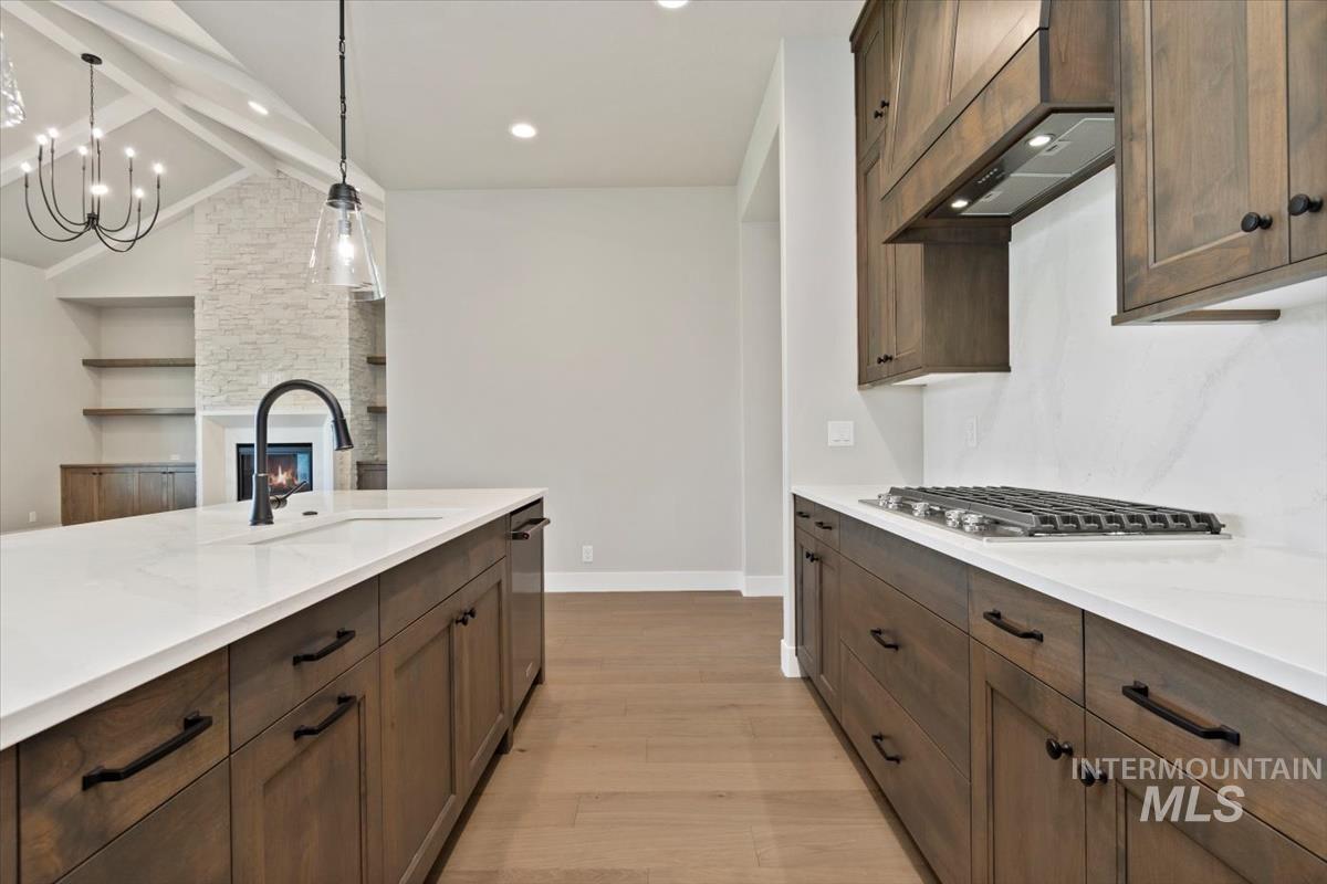 7353 Powell Place Eagle, ID 83714 - Photo 14 of 45 Kitchen featuring light wood-style flooring, dark brown cabinetry, a large fireplace, decorative light fixtures, and recessed lighting