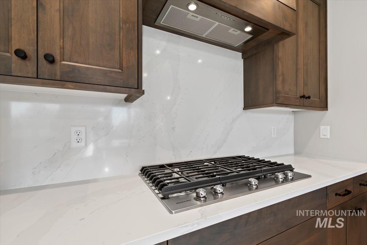 7353 Powell Place Eagle, ID 83714 - Photo 16 of 45 Kitchen with stainless steel gas stovetop, extractor fan, dark brown cabinetry, tasteful backsplash, and light stone counters