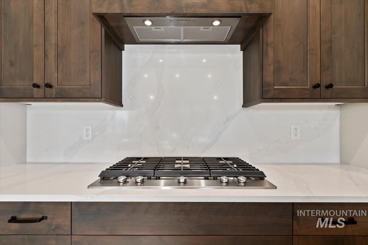 7353 Powell Place Eagle, ID 83714 - Photo 17 of 45 Kitchen featuring ventilation hood, stainless steel gas stovetop, dark brown cabinets, decorative backsplash, and light stone counters