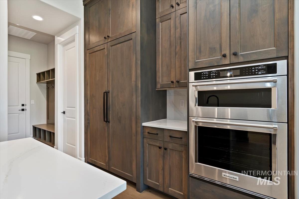 7353 Powell Place Eagle, ID 83714 - Photo 18 of 45 Kitchen featuring double oven, light stone counters, dark brown cabinetry, recessed lighting, and light wood finished floors