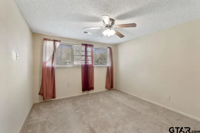 an empty room with chandelier fan and windows