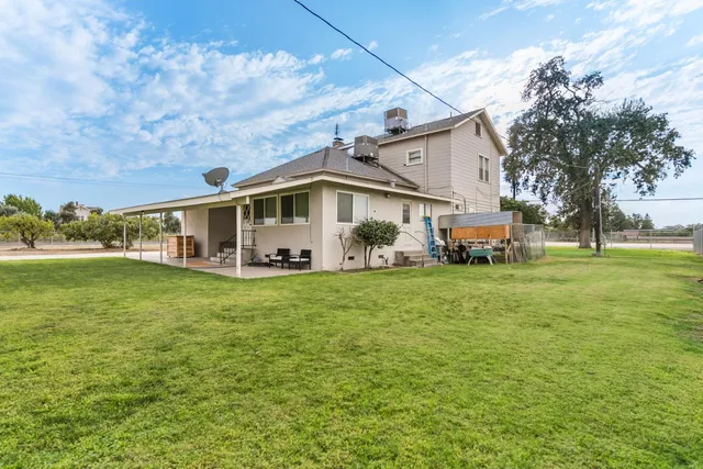 a view of a white house in front of a big yard with plants and large trees