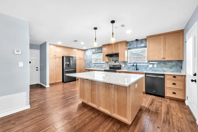 a large kitchen with stainless steel appliances granite countertop a stove a sink dishwasher and a refrigerator with wooden floor