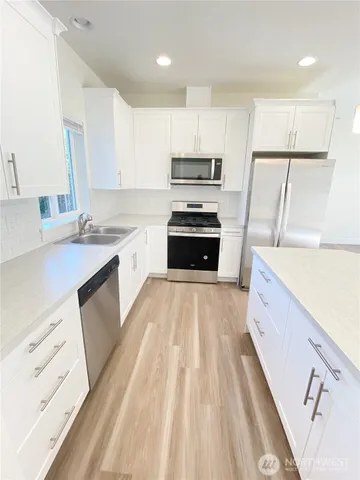 a large kitchen with stainless steel appliances granite countertop a refrigerator a sink dishwasher a stove and white countertops with wooden floor