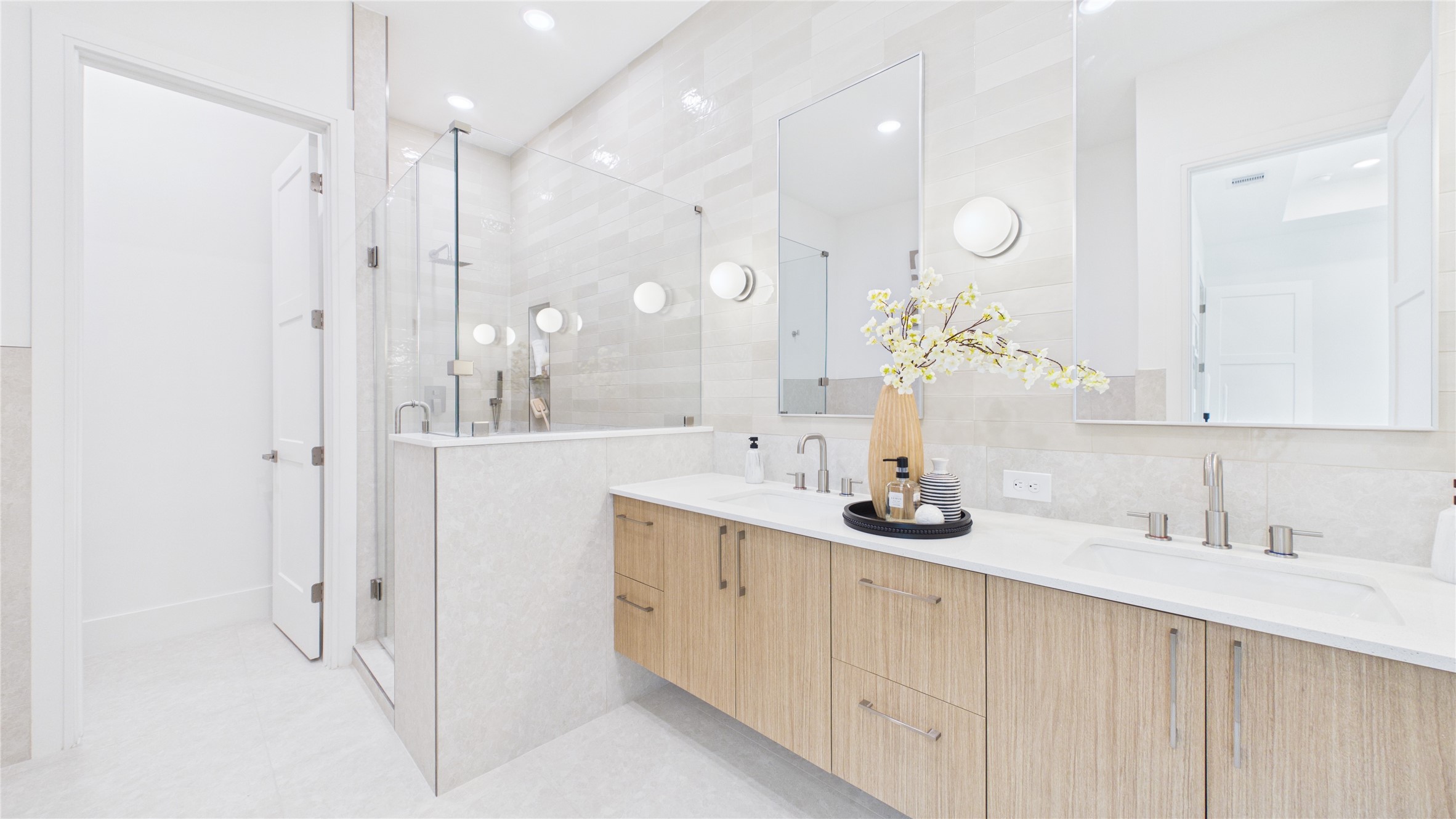 602 Skyland Terrace Way Houston, TX 77009 - Photo 30 of 40 This bright and modern bathroom features a double vanity with sleek wooden cabinets, large mirrors, and contemporary fixtures. A spacious glass-enclosed shower complements the clean, minimalist design, enhanced by soft lighting and elegant tile work.
