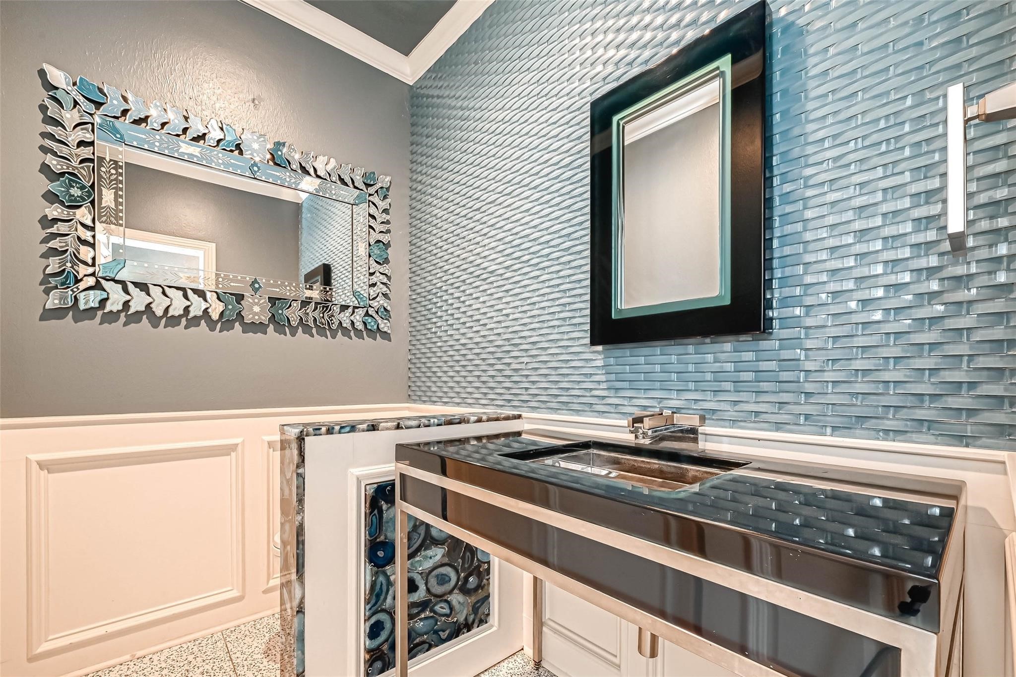 263 Wood Loop Street Houston, TX 77015 - Photo 36 of 45 This bathroom features a modern design with a sleek glass sink and chrome fixtures. The walls are adorned with textured blue tiles, and there's a decorative mirror adding elegance to the space. A stylish countertop complements the contemporary aesthetic.