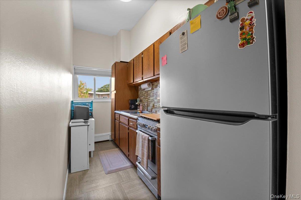 267 North Newbridge Road, Unit 2D Levittown, NY 11756 - Photo 15 of 22 Galley kitchen featuring wood cabinetry, stainless steel appliances, and a tiled backsplash