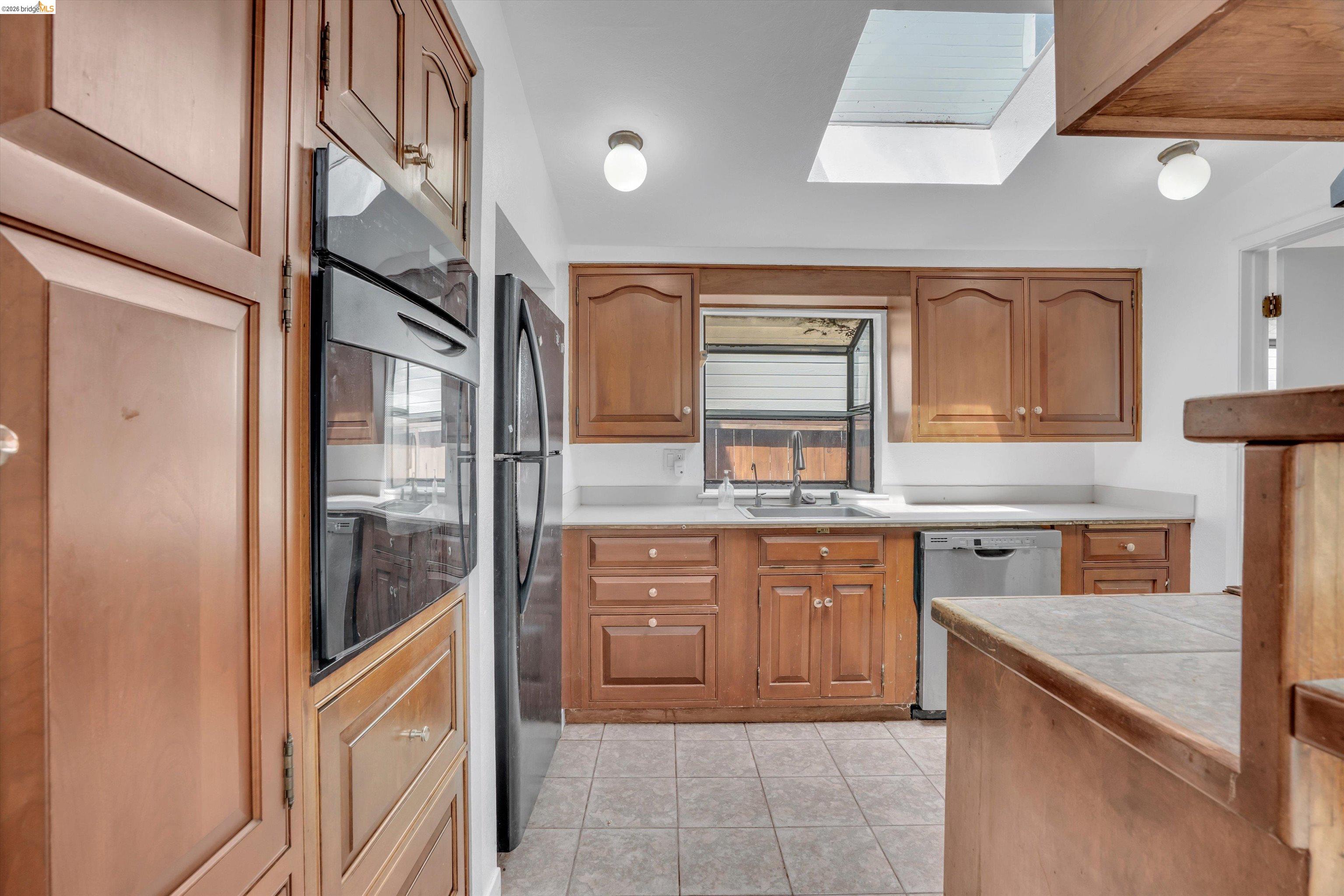 1922 Taylor Road Bethel Island, CA 94511 - Photo 27 of 49 Kitchen with a skylight, black appliances, light tile patterned floors, and wood finish cabinets