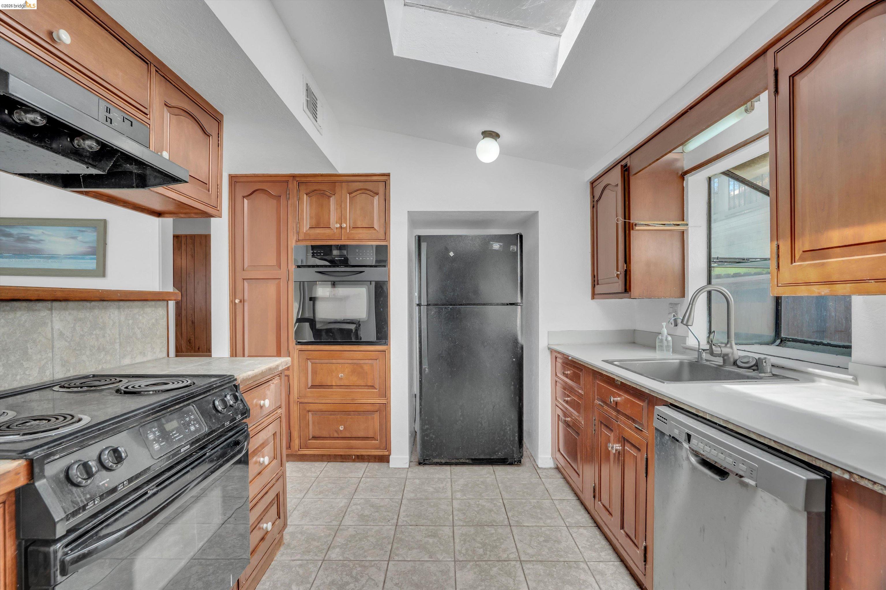 1922 Taylor Road Bethel Island, CA 94511 - Photo 29 of 49 Kitchen featuring black appliances, exhaust hood, light countertops, a skylight, and vaulted ceiling