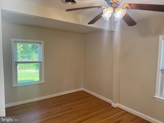 an empty room with wooden floor fan and windows