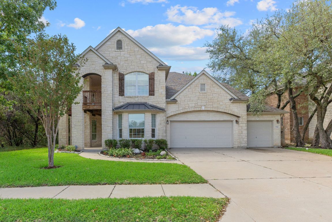 French country home with a front yard, concrete driveway, a garage, stone siding, and a balcony