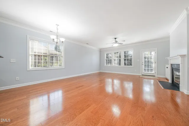 an empty room with wooden floor chandelier and windows