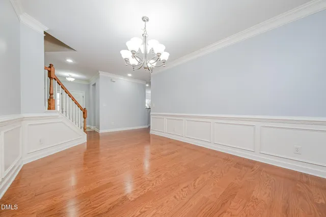 a view of an empty room with wooden floor and a kitchen