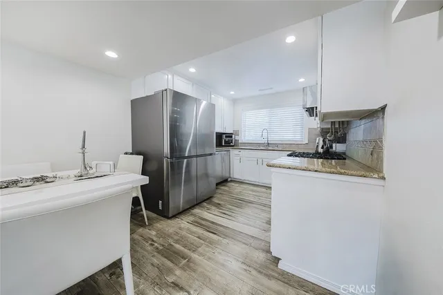 a kitchen with stainless steel appliances granite countertop a refrigerator a sink dishwasher a stove with white cabinets and wooden floor