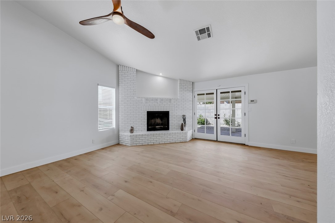 434 Crestway Road Henderson, NV 89015 - Photo 19 of 46 Unfurnished living room with french doors, ceiling fan, light wood-style flooring, a brick fireplace, and lofted ceiling