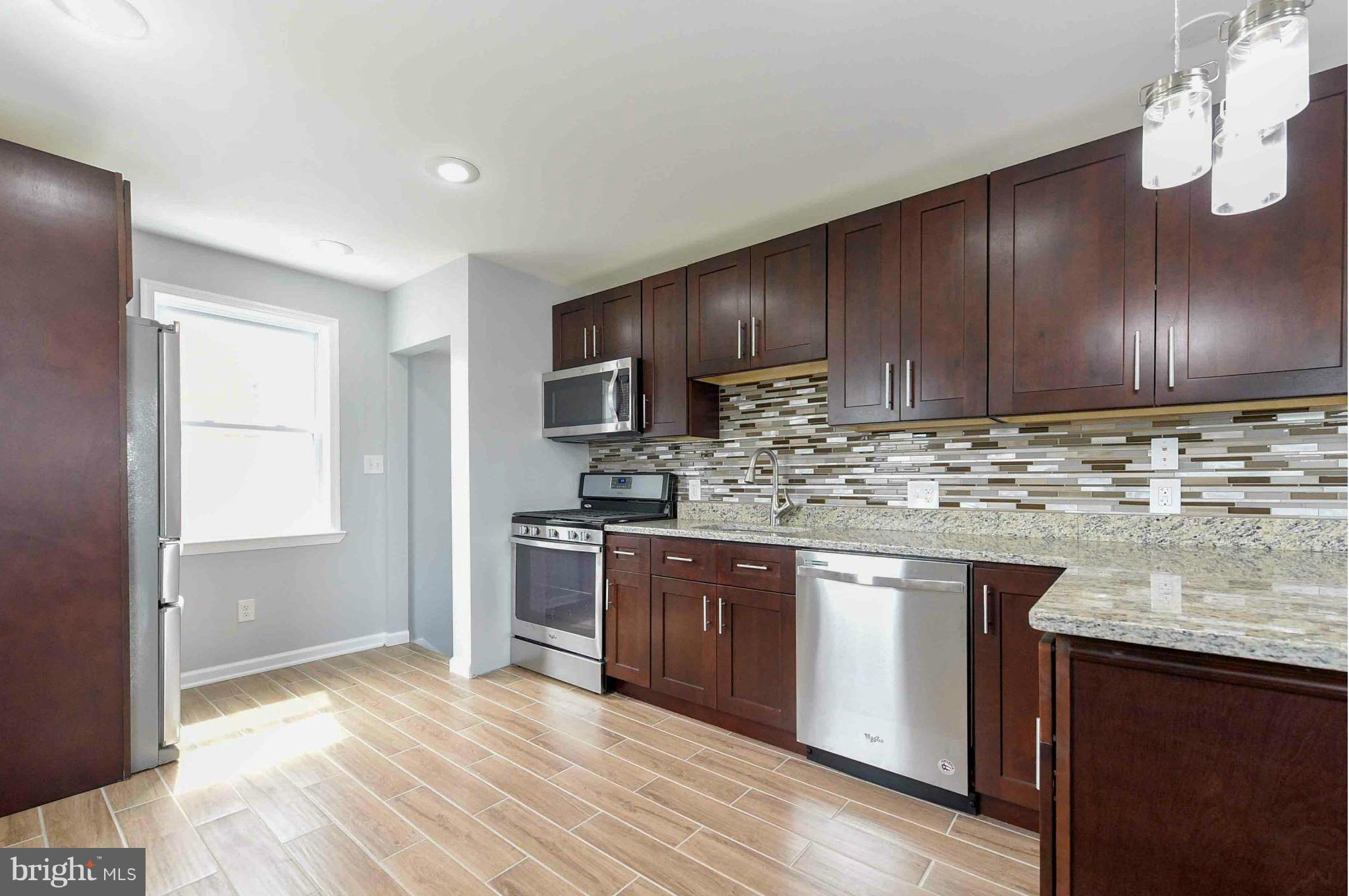 3822 Byfield Road Baltimore, MD 21207 - Photo 3 of 30 a kitchen with stainless steel appliances granite countertop wooden cabinets a stove top oven a sink and dishwasher with wooden floor