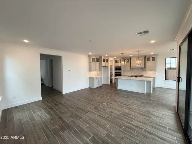 a view of an empty room with wooden floor and a kitchen