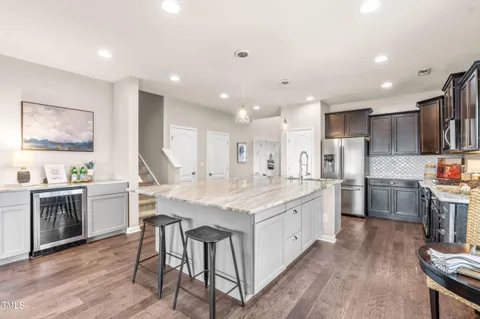a kitchen with stainless steel appliances granite countertop a stove top oven a sink dishwasher a refrigerator and a dining table with wooden floor