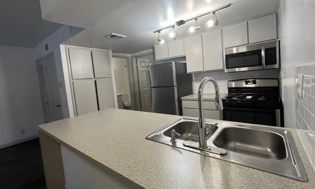 a kitchen with stainless steel appliances a sink a microwave a refrigerator and white cabinets