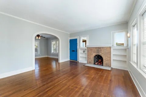 a view of an empty room with wooden floor fireplace and a window