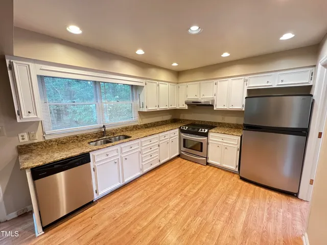 a kitchen with granite countertop a refrigerator a sink dishwasher and white cabinets with wooden floor