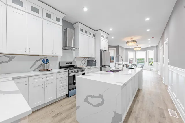 a large white kitchen with kitchen island a sink a stove a refrigerator and a dining table with wooden floor