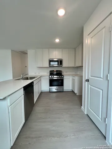 a large white kitchen with granite countertop a sink and dishwasher a stove with wooden floors