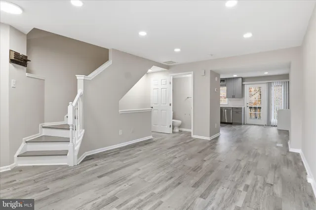a view of an empty room with wooden floor and kitchen