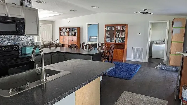 a kitchen with stainless steel appliances kitchen island granite countertop a dining table chairs and a refrigerator