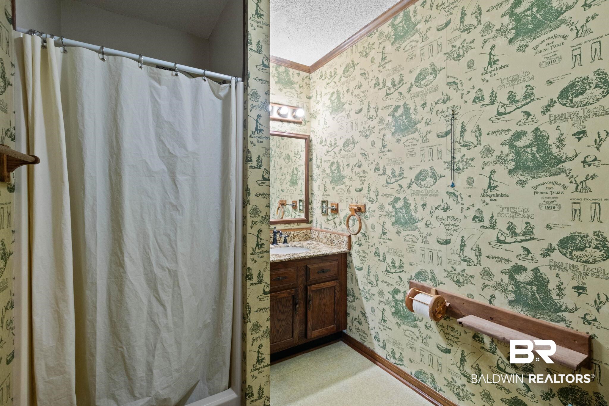 8153 Bryant's Lndg Road Stockton, AL 36579 - Photo 39 of 87 Bathroom featuring patterned wallpaper, a wood-finish vanity with a light-toned countertop, a rectangular mirror with a three-light fixture above, and a shower area with a curtain rod