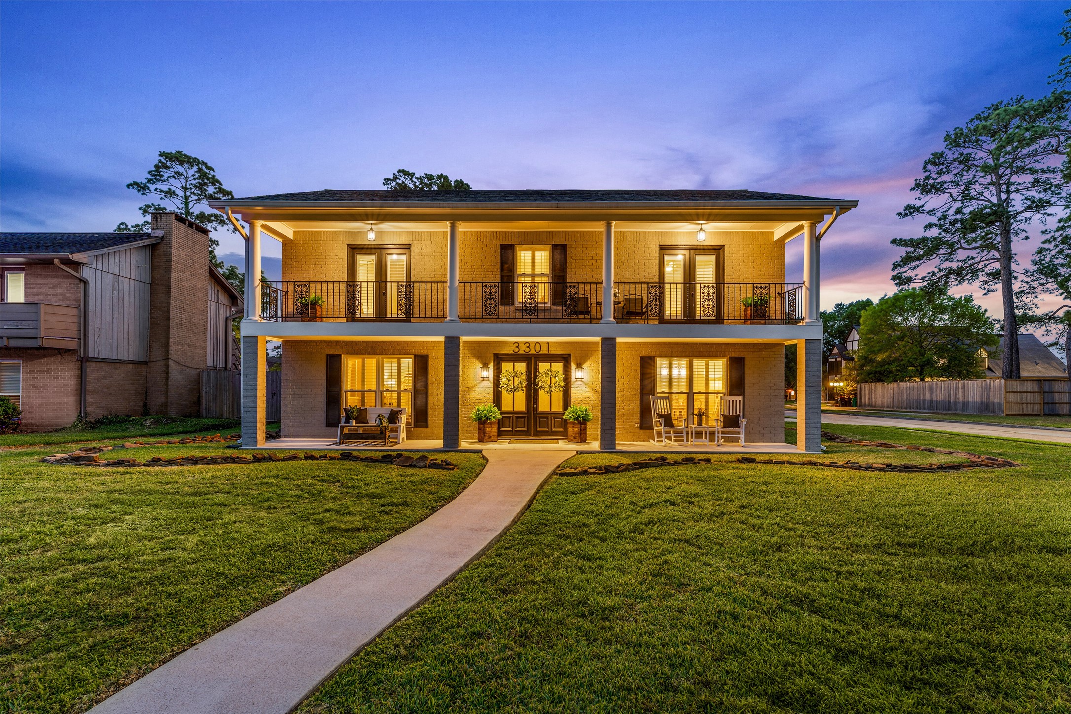 Corner lot, showcases a charming two-story home with a welcoming front porch and balcony, beautifully lit at twilight. The house is surrounded by a well-maintained lawn and is situated close to walking trails and parks.